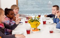 Sechs Kinder sitzen im Aufenthaltsraum der Museumsherberge und trinken Traubensaft und knabbern Möhren