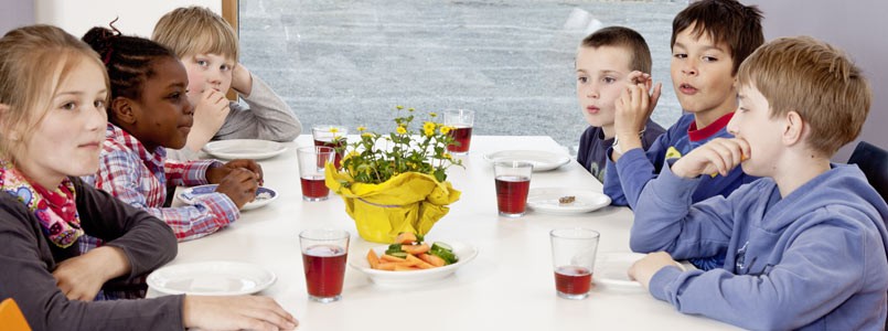 Sechs Kinder sitzen im Aufenthaltsraum der Museumsherberge und trinken Traubensaft und knabbern Möhren