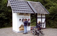 Eine Besucherin im Rollstuhl mit Elektroantrieb vor den Insektenhotels und Nistkästen