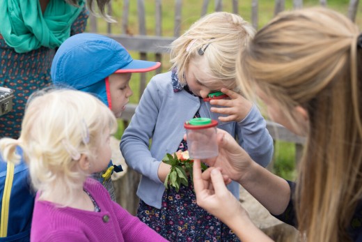 Eine Frau zeigt mehreren Kindern wie sie mit einer Lupe und einem Beobachtungsgefäß Dinge aus der Natur betrachten können.