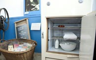 Ein Weidenkorb ist gefüllte mit alten Waschmittelpackungen. Daneben steht ein alter weißer Kühlschrank mit geöffneter Tür.