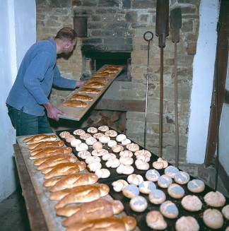 Der Museumsbäcker im Backhaus aus Overath-Kepplerburg: Er holt ein Blech mit frisch gebackenen Weckmännern aus dem Ofen, der zuvor mit einem Holzfeuer angeheizt wurde. Im Vordergrund sind schon fertige Backwaren zu sehen. Weitere Brötchen warten noch aufs Backen.
