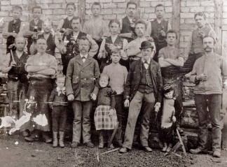 Arbeiter, Hilfskräfte und Kinder posieren auf einer alten schwarz-weiß-Aufnahme für den Fotografen. Die Aufnahme entstand um 1910