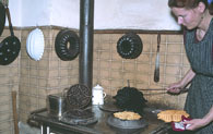 Die Hauswirtschafterin backt auf der 'Kochmaschine'  Waffeln mit einem gusseisernen Waffeleisen. Der Ofen wird mit Holz und Kohle befeuert.