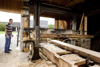 Blick aus dem Inneren des Sägegatters. Ein Handwerker überwacht den einwandfreien Betrieb der Säge