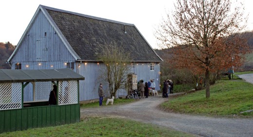 Besucher stehen vor der Scheune aus Reichshof-Denklingen. Im Vordergrund steht ein Gartenpavillon.