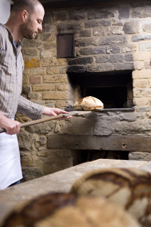 Der Museumsbäcker holt mit einem Holzschieber das frisch gebackene Brot aus dem gemauerten Backofen.