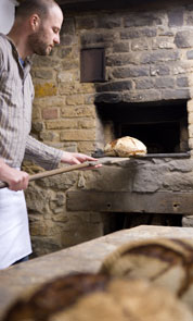 Der Museumsbäcker holt mit einem Holzschieber das frisch gebackene Brot aus dem gemauerten Backofen.
