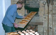 Der Bäcker zieht ein Blech mit Weckmännern aus dem Holzofen im historischen Backhaus.