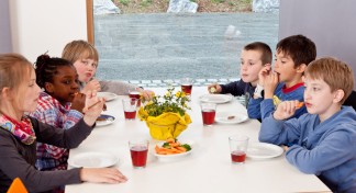 Sechs Kinder sitzen im Aufenthaltsraum der Museumsherberge und trinken Traubensaft und knabbern Möhren