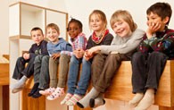 Sechs Kinder sitzen in der oberen Etage eines Etagenbettes und lassen die Füsse über den Rand baumeln.