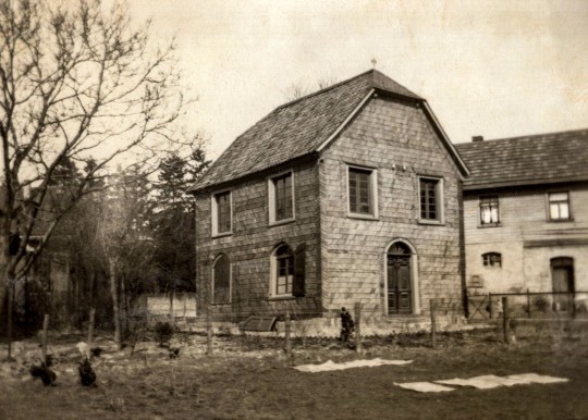 Historisches Foto der Synagoge in Nümbrecht um 1925. Das zweistöckige Gebäude im Bergischen Stil ist umgeben von Bäumen.