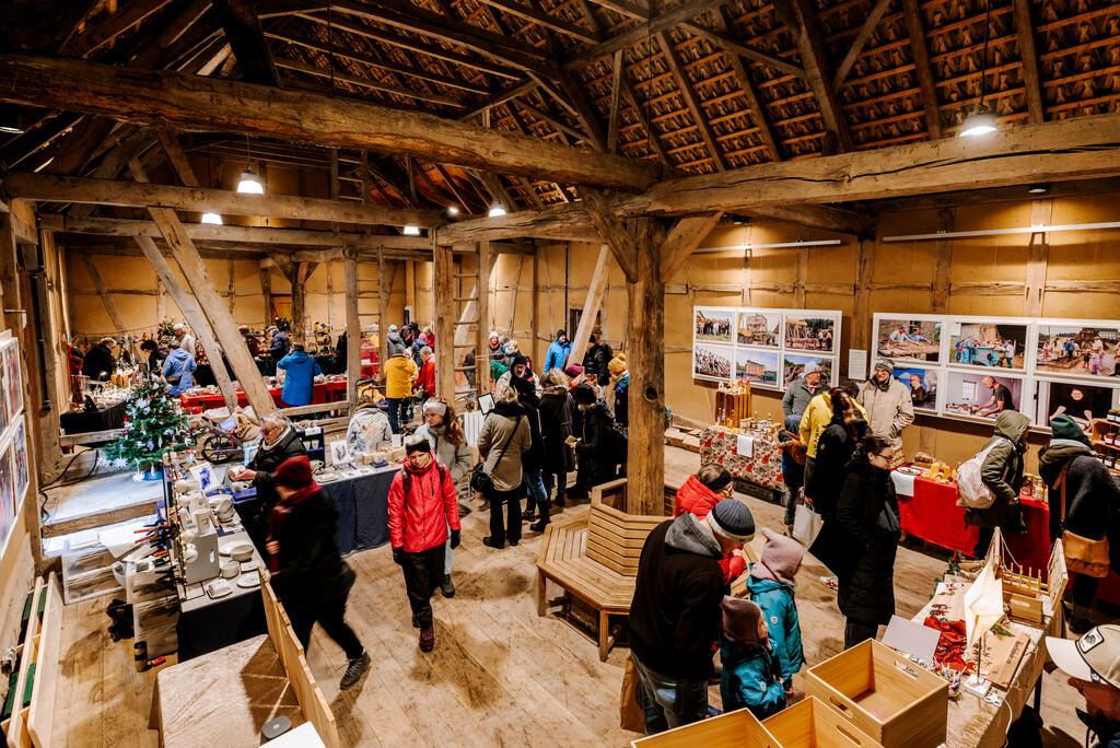 In der Zehntscheune sind mehrere Stände mit regionalen Adventsprodukten aufgebaut. Viele Besuchende schlendern durch die Scheune und betrachten die Waren.
