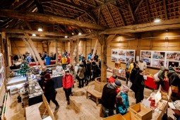 In der Zehntscheune sind mehrere Stände mit regionalen Adventsprodukten aufgebaut. Viele Besuchende schlendern durch die Scheune und betrachten die Waren.