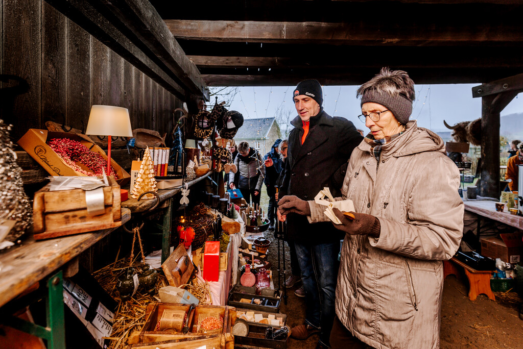 Mehrere Besuchende an einem der weihnachtlichen Vekaufsstände in einer der Scheunen. Links sind eine ganze Reihe an unterschiedlichen Waren zu sehen.